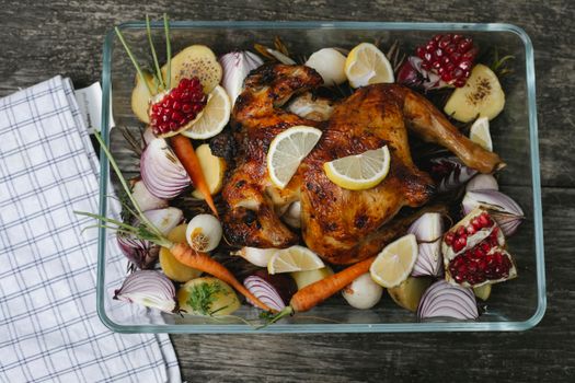 Plat de poulet rôti avec légumes colorés et quartiers de citron, servi dans un plat en verre.