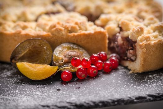 Crumble cake aux fruits, avec des prunes et des groseilles sur une planche en ardoise, saupoudré de sucre glace.