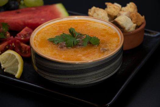 Bol de soupe orange garni de coriandre, accompagné de fruits frais et de croûtons sur un plateau noir.