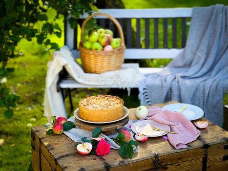 Crumble cake sur une table en bois, avec des pommes et des fleurs, dans un jardin ensoleillé.